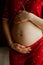 Photo closeup of pregnant woman in cute red pajamas touching with hands big bare tummy. Female body. Motherhood concept.