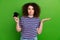 Photo of clueless young person hold controller raise arm shrug shoulder isolated on green color background