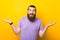 Photo of a confused bearded man is shrugging over yellow background.