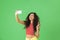 Photo of content woman smiling and using cell phone for selfie isolated over green background