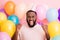Photo of crazy funky dark skin guy enjoy birthday surprise raise fists surrounded many air balloons rejoicing wear paper