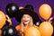 Photo of crazy small witch lady halloween party hiding between many air balloons excited evening wear orange t-shirt