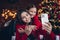 Photo of cute adorable little siblings dressed red sweaters cuddling recording video vlog modern device indoors