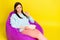 Photo of cute brown hairdo millennial lady sit on bag eat pop corn wear hoodie trousers  on yellow background