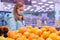 Photo of a cute girl in a medical mask and gloves choosing tangerines in the supermarket. Shopping in compliance with