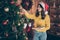 Photo of cute nice good kind girl decorating while wearing yellow pullover denim red cap jeans feeling festive