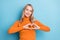 Photo of cute shiny young lady wear orange sweater showing fingers heart smiling isolated blue color background