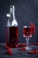 Photo in dark style: glass and bottle of red currant drink. A bunch of currants on a beautiful glass goblet