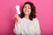 Photo of delighted charismatic young lady posing isolated over pink background in studio, raising one hand, holding hygiene pad,