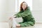 Photo of delighted red haired female stretches legs, has fitness training, wears sportshoes and tracksuit, has glad expression,