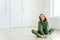 Photo of delighted redhead female sits on lotus pose, wears tracksuit, being in good body shape, has curly ginger hair, poses on