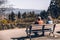 The photo depicts a senior couple sitting on a bench inside Queen Elizabeth Park in Vancouver