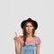 Photo of displeased woman farmer wears casual overalls, stylish black hat, points at upper corner, feels dissatisfid