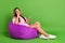 Photo of doubtful unsure woman dressed t-shirt sitting bean bag looking empty space typing modern device isolated green