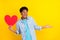 Photo of dreamy impressed dark skin guy dressed denim shirt looking empty space holding heart isolated yellow color