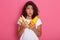 Photo of emotional shocked female with dark wavy hair, holds corn and zucchini looks directly at camera, keeps mouth opened, lady