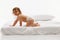 Photo of energetic toddler, little girl crawling on the bed in midst of fun day against white background. Textile and