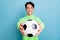 Photo of excited sweet young guy dressed green hoodie inviting play football smiling isolated blue color background