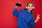 Photo of fascinating happy smiling young woman wearing stylish blue hoodie isolated over red background wearing white