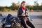 Photo of female driver holds smart phone in hands, surfes bikers blog in internet, wears stylish clothes, leans at black fast moto