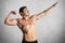 Photo of fit strong young male bodybuilder poses, shows flexed muscles, stretches hands, isolated over grey background. Fitness mo