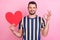Photo of flirty young brunet guy hold heart show okey wear striped t-shirt isolated on pink color background