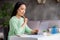 Photo of focused asian girl sit cozy desk work study remote prepare report hold pen copybook look laptop screen in house