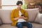 Photo of focused calm handsome guy hold telephone look screen texting sit couch wear yellow shirt home indoors