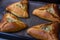 Photo of four ruddy triangular pies on a baking sheet, just taken out of the oven