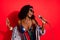 Photo of funky charming curly dark skin woman dressed pinup clothes spectacles singing karaoke isolated red color