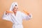 Photo of funky happy young lady hold bottles dance wear bathroom turban robe isolated on pastel beige color background