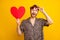 Photo of funky impressed young guy wear leopard outfit arm dark eyewear holding red heart isolated yellow color
