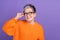 Photo of funky thoughtful woman dressed orange sweater arm eyewear looking empty space isolated violet color background