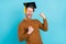 Photo of funny adorable guy dressed knit sweater academic hat spectacles screaming rising fists isolated blue color