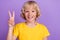 Photo of funny excited friendly boy show v-sign wear yellow t-shirt  purple color background