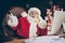 Photo of funny grey beard santa claus sit table call speak telephone have x-mas christmas gift present delivery