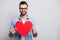 Photo of funny handsome guy holding large red paper heart inviting girlfriend romantic date tender emotions wear specs