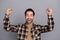 Photo of funny lucky guy dressed checkered shirt smiling rising fists isolated grey color background