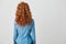 Photo of girl with red curly hair standing back to camera over white background. Copy space.