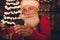 Photo of grandpa santa claus look phone screen delivery service order wear hat sweater in north pole office indoors