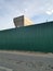 Photo of green zinc fence on asphalt road and partially concrete pillar in the morning