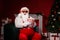 Photo of grey bearded santa claus sit in chair hold pop corn box with christmas evergreen tree fireplace x-mas ornament