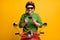 Photo of guy ride moped showing plastic card wear helmet spectacles green sweater isolated yellow color background