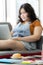 Photo of hamburger in a white plate on a table with a blur background of fat woman sitting on a couch working on a computer