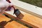 Photo of a hand painting a wooden beam with brown glazing varnish. Brush in the hands of the painter.