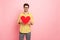 Photo of handsome guy holding large red paper heart symbolizing sincere feelings calling girlfriend to prom wear specs