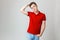 Photo of handsome guy wearing red shirt and blue jeans smiling standing over white background with boring facial