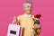 Photo of handsome mature man with grey hair, wears elegant yellow shirt, bowtie, holds bouquet of red roses and pink bag with