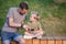 Photo of happy man and boy with phones in hands sitting behind wooden fence in park