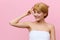 photo of a happy, sophisticated woman with blonde hair gathered back, standing on a pink background, wiping her face